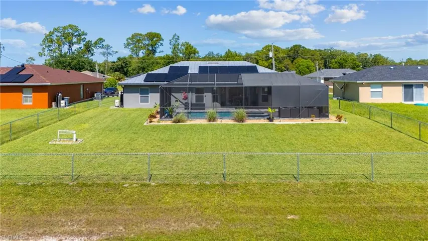 Back of property with glass enclosure, a yard, solar panels, and a fenced in pool