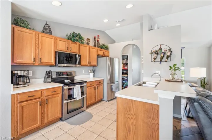 Kitchen with lofted ceiling, stainless steel appliances, a kitchen island with sink, sink, and light tile floors