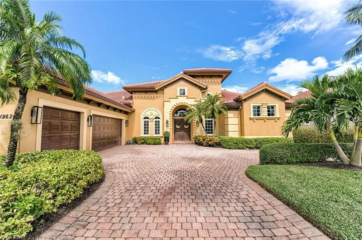 Stucco exterior with a tile roof, paver driveway, arched entry, two-car garage, and established landscaping