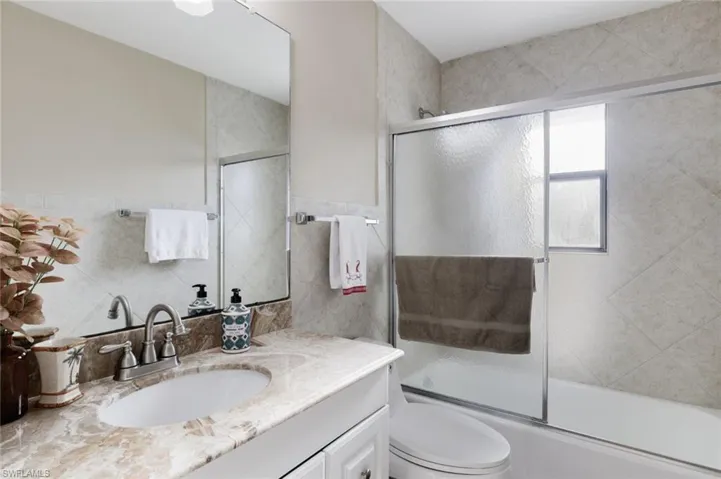 Full bathroom with vanity, tile walls, and bath / shower combo with glass door