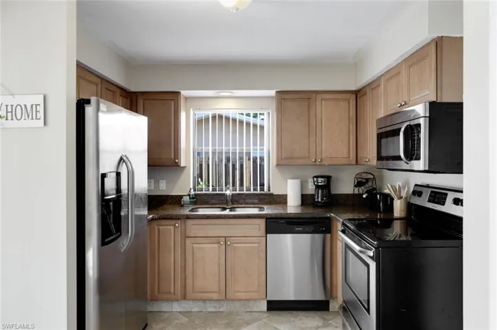 Kitchen featuring appliances with stainless steel finishes, dark stone counters, and light tile patterned floors