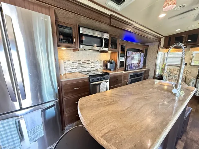Kitchen featuring stainless steel appliances, light countertops, a center island, glass fronted cabinets, and dark wood finish cabinets