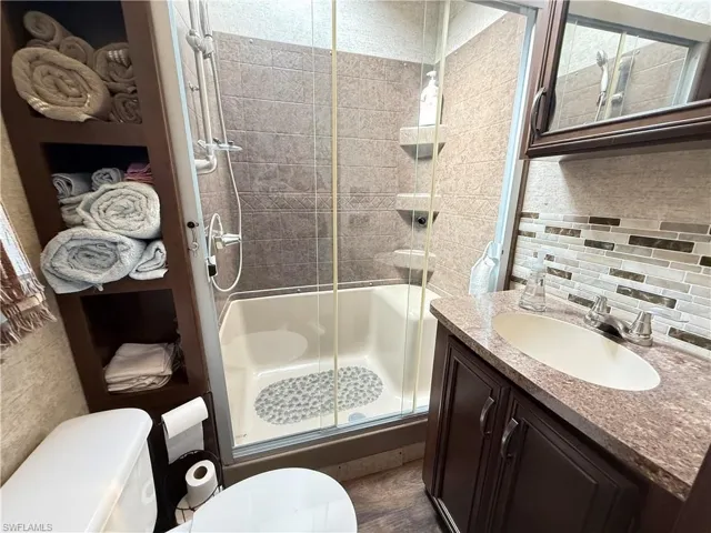 Full bath featuring decorative backsplash, a stall shower, and vanity