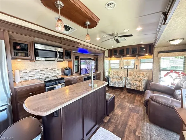 Kitchen with pendant lighting, stainless steel appliances, dark wood finish cabinetry, a ceiling fan, and glass insert cabinets