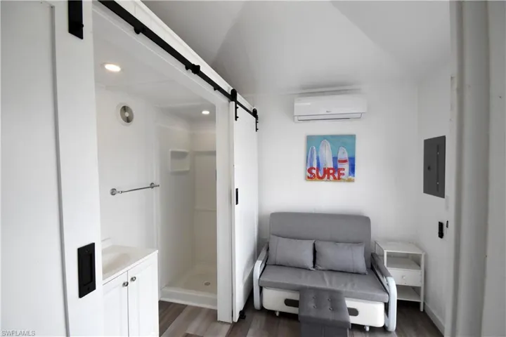 Living area with an AC wall unit, a barn door, dark wood-type flooring, and electric panel