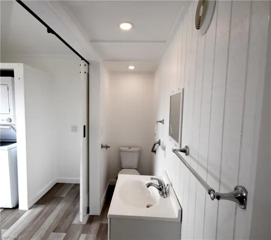 Bathroom with stacked washer and dryer, vanity, toilet, recessed lighting, and wood finished floors