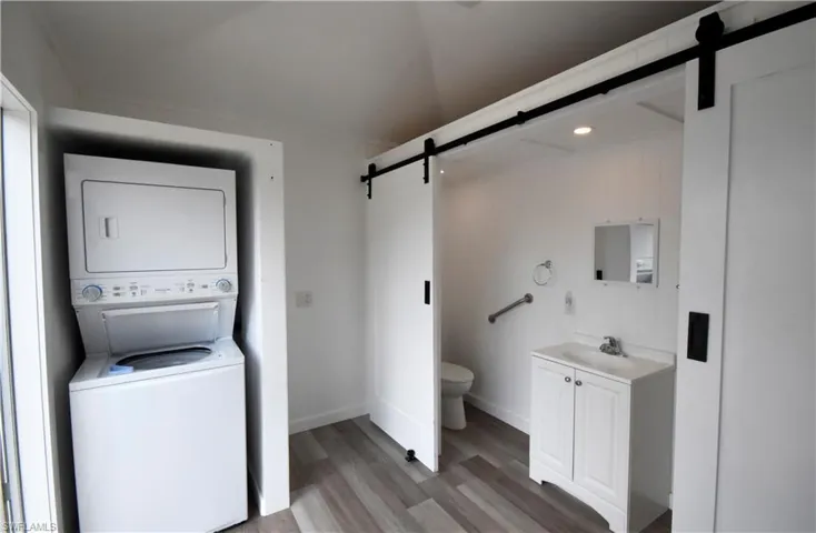 Bathroom featuring wood finished floors, vanity, baseboards, toilet, and stacked washer and clothes dryer