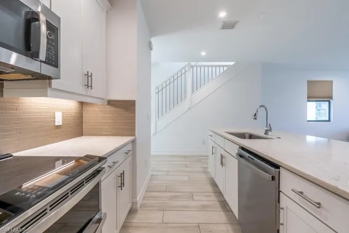 Kitchen featuring stainless steel appliances, white cabinetry, light stone countertops, wood tiled floors, and decorative backsplash
