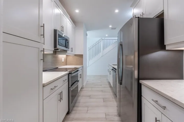 Kitchen with appliances with stainless steel finishes, white cabinetry, decorative backsplash, light stone counters, and recessed lighting