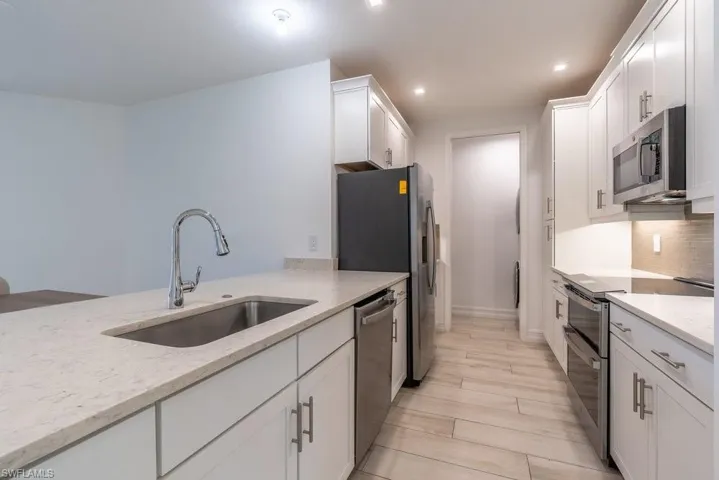 Kitchen with appliances with stainless steel finishes, white cabinetry, light stone countertops, wood finish floors, and recessed lighting