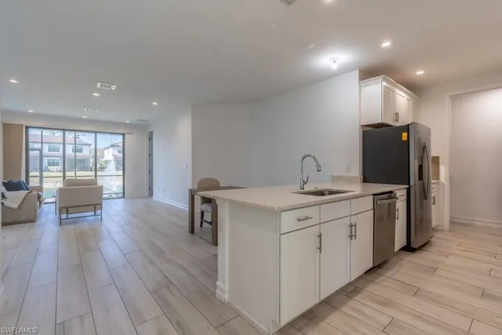 Kitchen with open floor plan, recessed lighting, white cabinets, wood finish floors, and light stone countertops