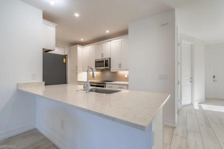 Kitchen with stainless steel appliances, white cabinets, a peninsula, light stone countertops, and tasteful backsplash