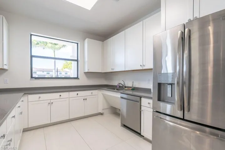 Clubhouse kitchen with stainless steel appliances, white cabinets, dark countertops, and light tile patterned floors