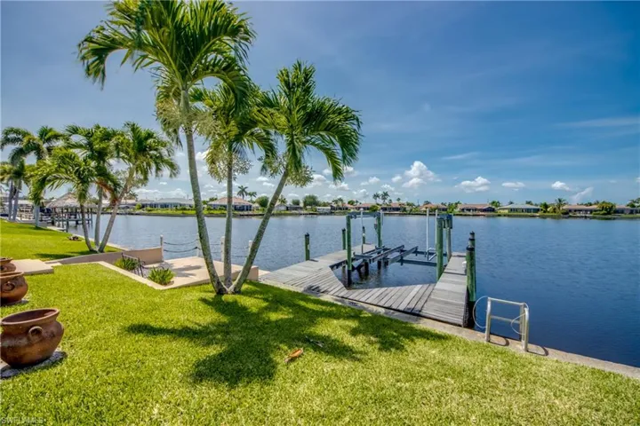 Dock featuring boat lift, a lawn, and a water view