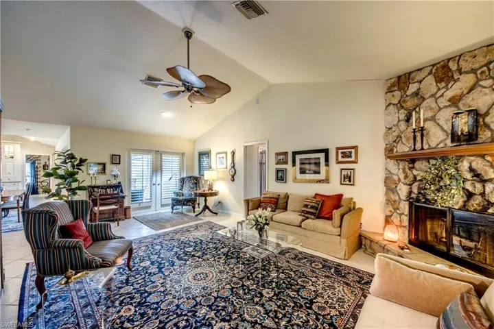Living room featuring ceiling fan, a stone fireplace, light tile patterned flooring, french doors, and high vaulted ceiling