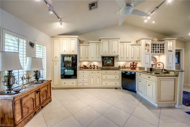 Kitchen with rail lighting, cream cabinets, black appliances, and vaulted ceiling