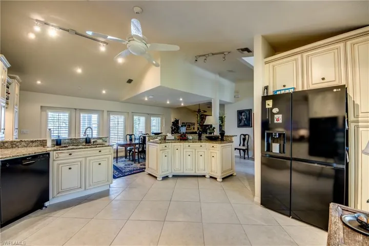 Kitchen with black appliances, cream cabinets, ceiling fan, light stone counters, and vaulted ceiling