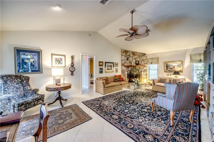 Living room featuring a ceiling fan, vaulted ceiling, a stone fireplace, and light tile patterned floors