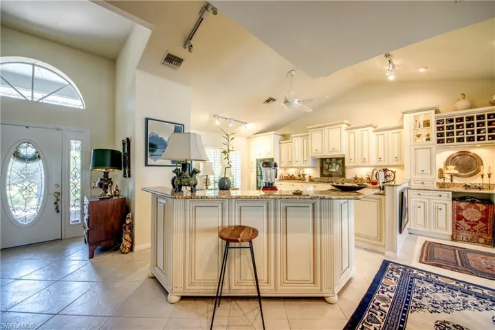 Kitchen featuring rail lighting, cream cabinets, healthy amount of natural light, light stone counters, and high vaulted ceiling
