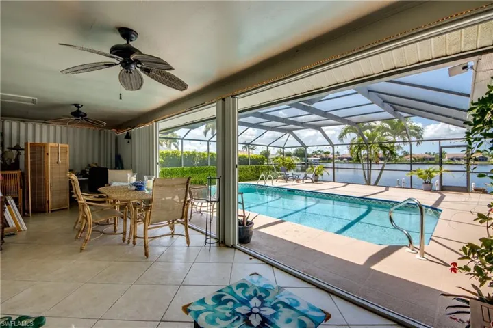 Swimming pool with ceiling fan, a patio area, a water view, outdoor dining area, and a lanai