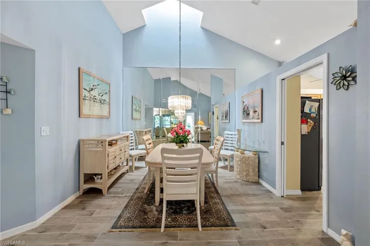 Dining space with a chandelier, wood finish floors, high vaulted ceiling, and a skylight