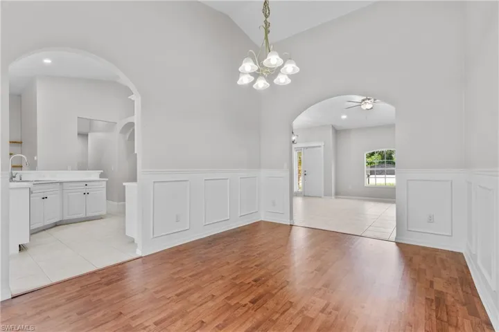 Spare room with high vaulted ceiling, light wood-style flooring, ceiling fan, arched walkways, and a wainscoted wall