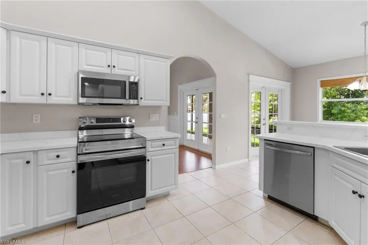 Kitchen featuring stainless steel appliances, vaulted ceiling, arched walkways, french doors, and light tile patterned floors