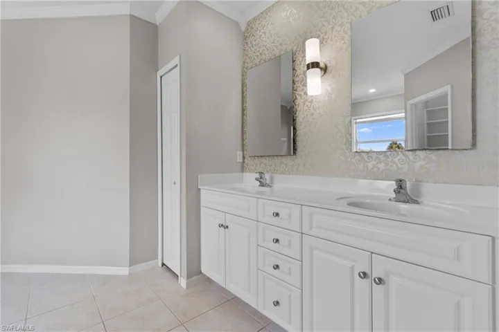Full bathroom with crown molding, double vanity, wallpapered walls, and tile patterned floors