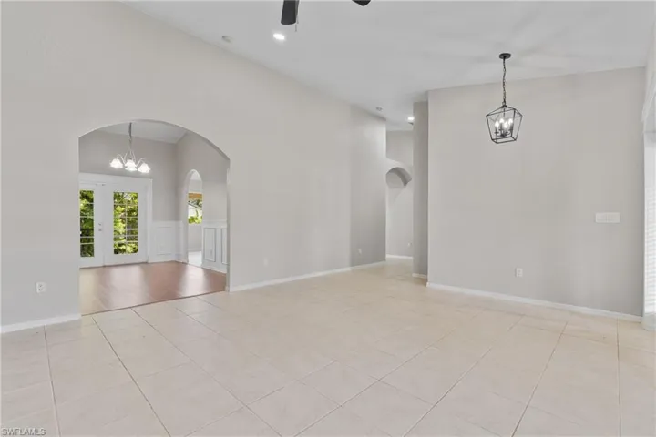 Empty room featuring a chandelier, light tile patterned floors, a towering ceiling, ceiling fan, and arched walkways