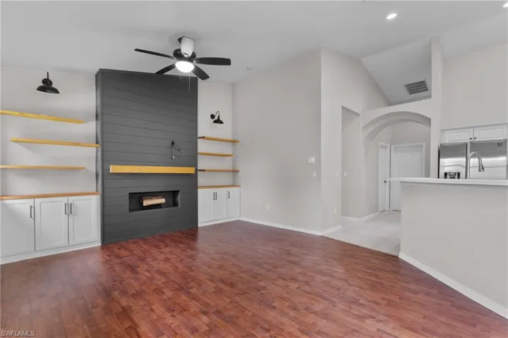 Unfurnished living room featuring ceiling fan, a large fireplace, light wood-style floors, vaulted ceiling, and arched walkways