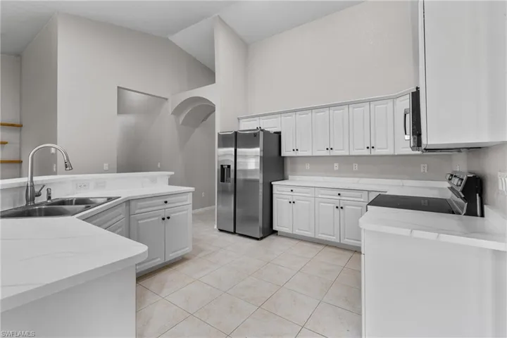 Kitchen featuring appliances with stainless steel finishes, light tile patterned flooring, high vaulted ceiling, white cabinetry, and light stone countertops