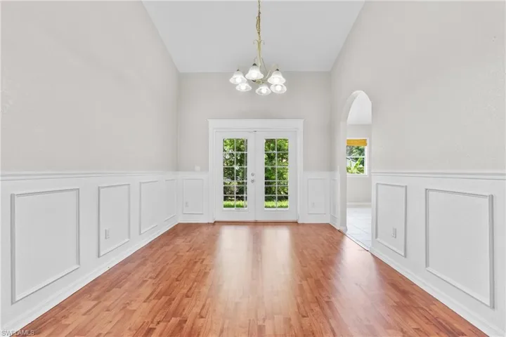 Unfurnished dining area featuring a chandelier, french doors, a wainscoted wall, light wood-type flooring, and a decorative wall