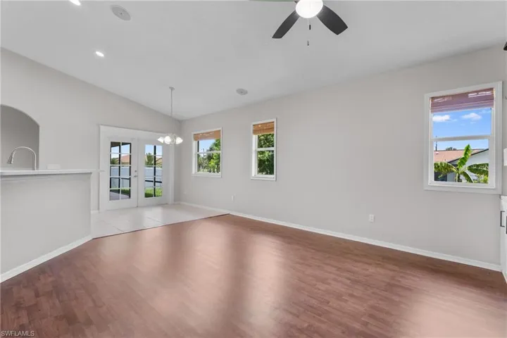 Empty room featuring ceiling fan, light wood-type flooring, french doors, vaulted ceiling, and a chandelier