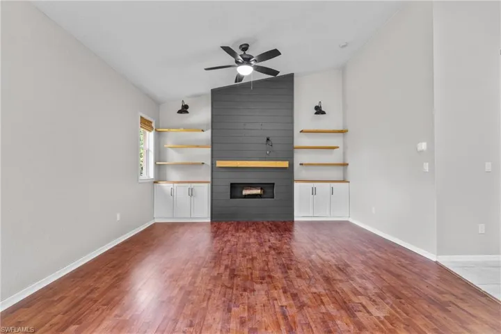 Unfurnished living room with vaulted ceiling, a fireplace, wood finished floors, and a ceiling fan