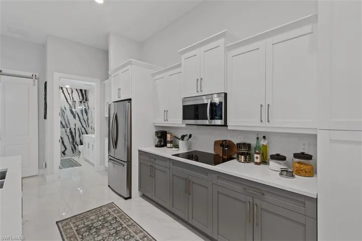 Kitchen with white cabinets, gray cabinets, appliances with stainless steel finishes, a barn door, and light stone countertops