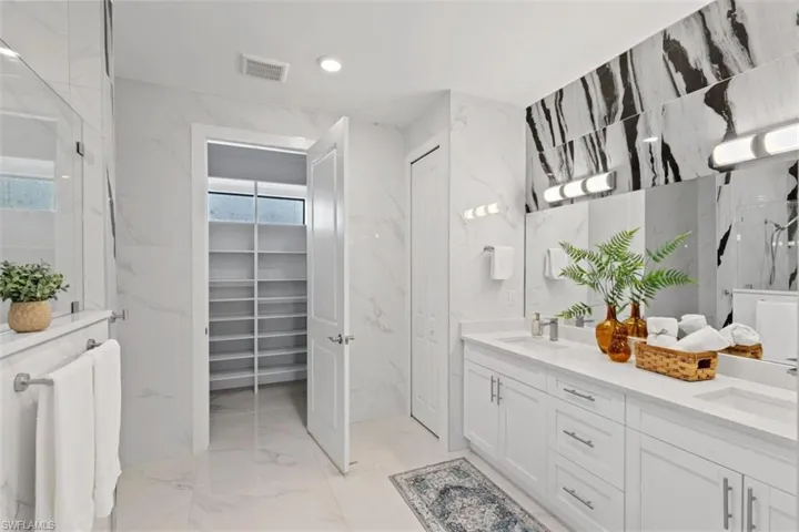 Full bath with stone wall, double vanity, a spacious closet, light marble finish flooring, and tile walls