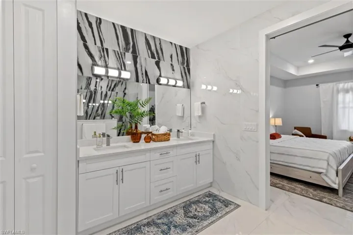 Ensuite bathroom with light marble finish floors, stone wall, double vanity, tile walls, and ceiling fan