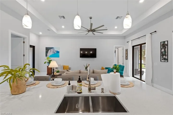 Kitchen with light stone countertops, pendant lighting, open floor plan, a raised ceiling, and recessed lighting