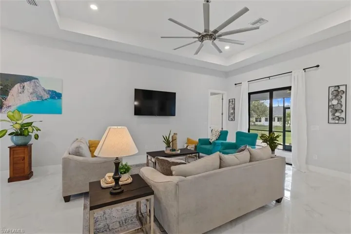 Living area featuring a raised ceiling, light marble finish floors, recessed lighting, and ceiling fan