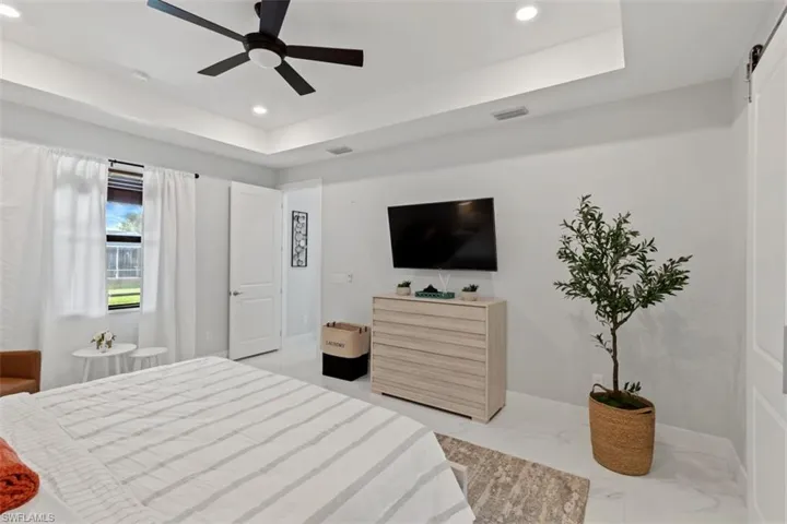 Bedroom featuring light marble finish flooring, a ceiling fan, a raised ceiling, recessed lighting, and a barn door