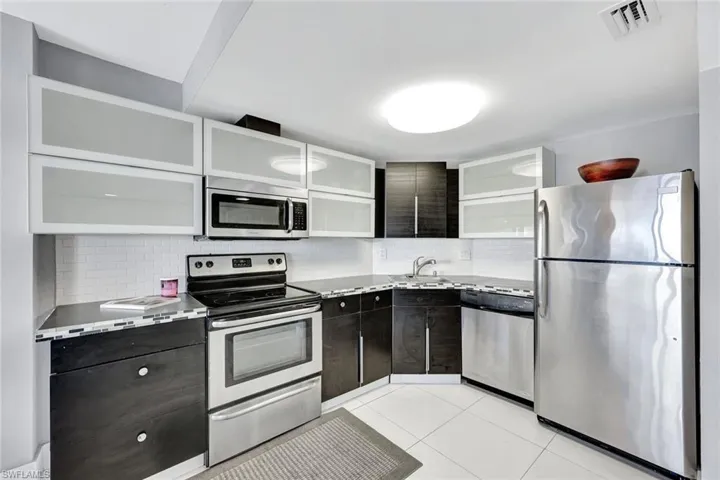 Kitchen featuring stainless steel appliances, backsplash, light tile patterned flooring, white cabinets, and modern cabinets