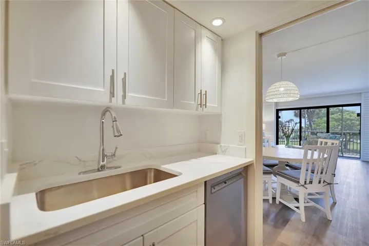 Kitchen with white cabinetry, stainless steel dishwasher, dark wood-style floors, light stone countertops, and decorative light fixtures