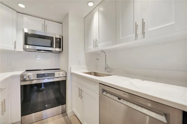Kitchen with appliances with stainless steel finishes, white cabinetry, tasteful backsplash, light stone counters, and light wood finished floors