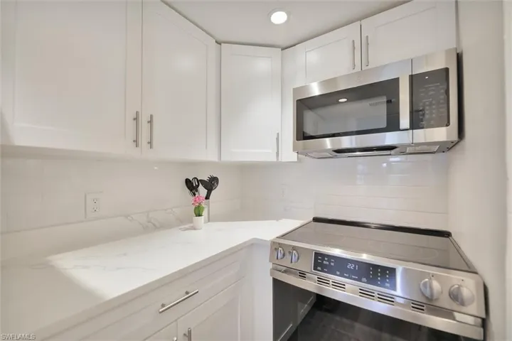 Kitchen featuring decorative backsplash, stainless steel appliances, white cabinets, and light stone counters
