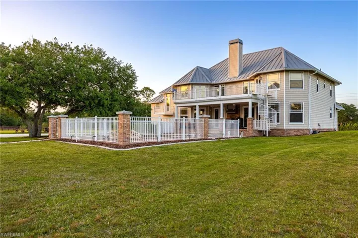 Rear view of house featuring a standing seam roof, a lawn, metal roof, fence, and a chimney
