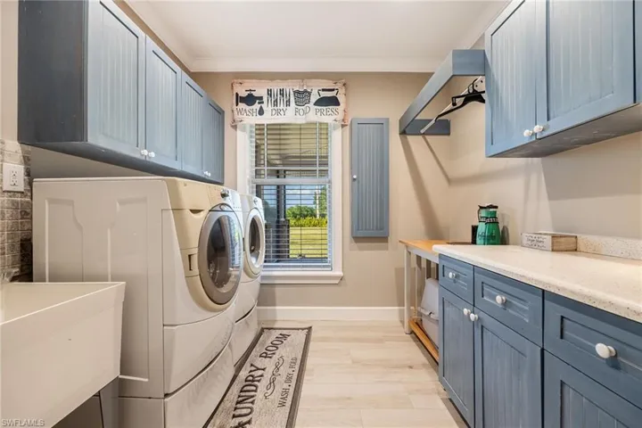 Laundry room featuring baseboards, crown molding, washer and clothes dryer, cabinet space, and light wood finished floors