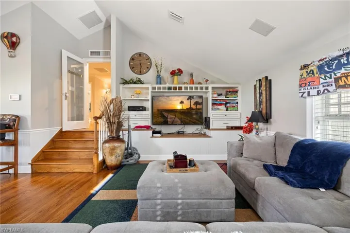 Living room featuring wainscoting, wood finished floors, lofted ceiling, and visible vents
