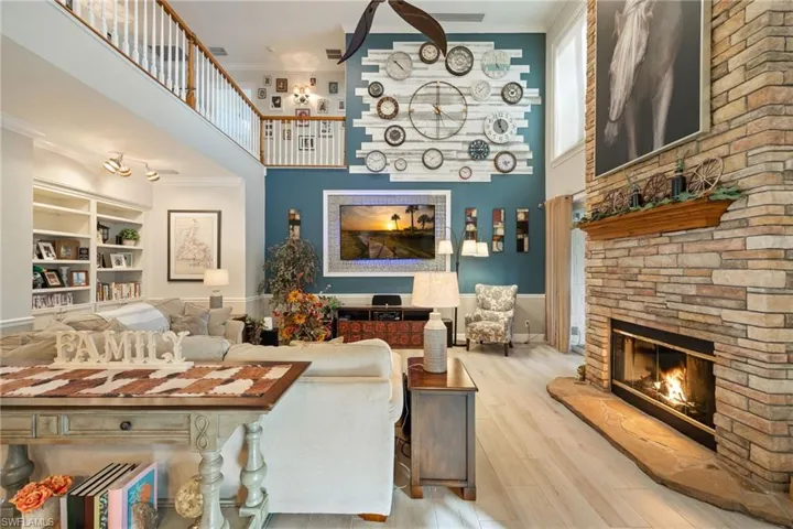 Living room with wood finished floors, a towering ceiling, ornamental molding, and a stone fireplace