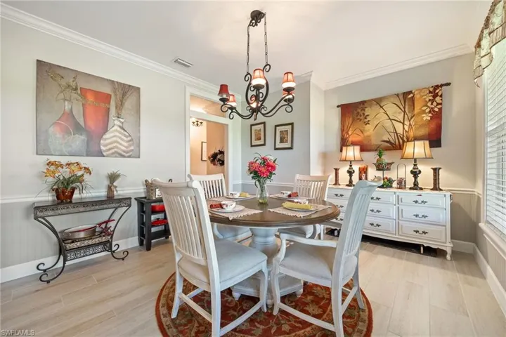 Dining room featuring light wood-style flooring, ornamental molding, visible vents, a chandelier, and wainscoting