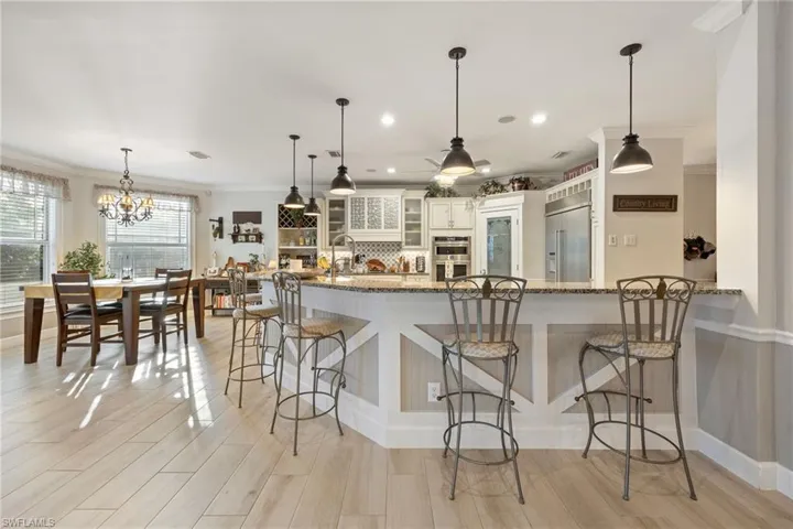 Kitchen featuring a kitchen breakfast bar, light wood-type flooring, glass insert cabinets, backsplash, and appliances with stainless steel finishes